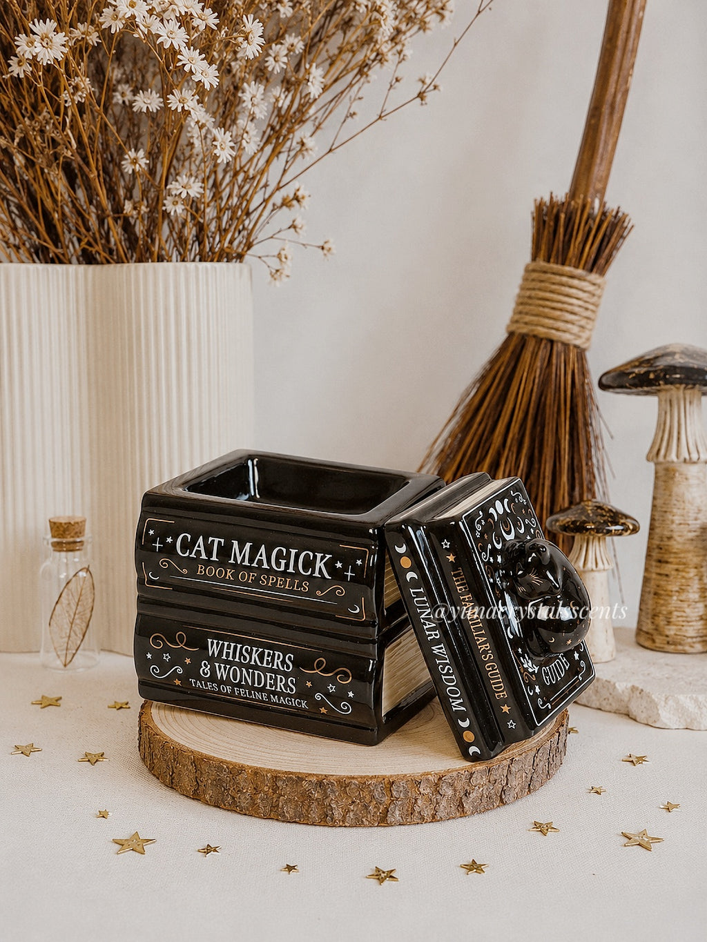 Decorative black box with text on a wooden surface with dried flowers and a broom in the background.